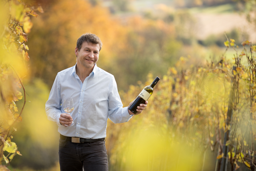 Martin Zieger im Weingarten mit einer Flasche Rotwein
